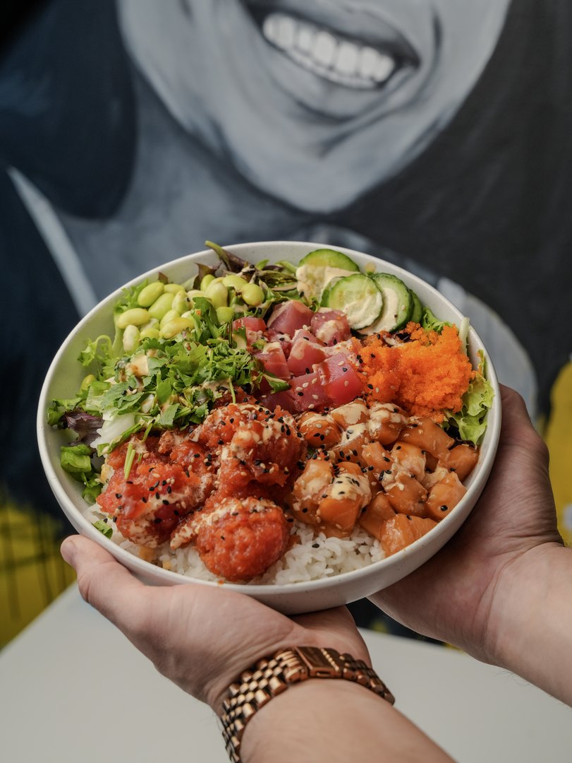 Pokitomik poke bowl held up in front of a mural